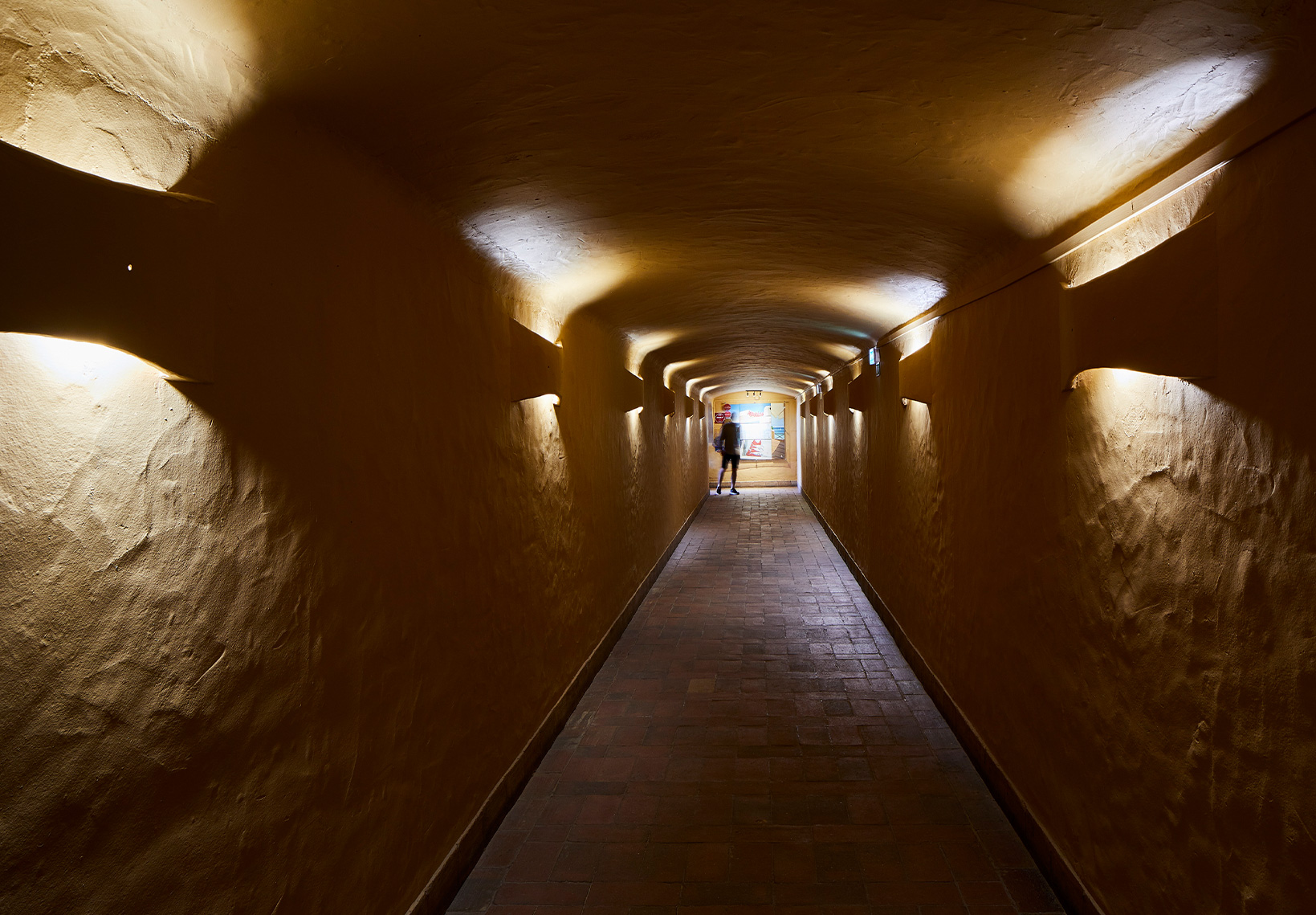 Túnel de acesso iluminado por luzes de parede quentes conduzindo ao restaurante.