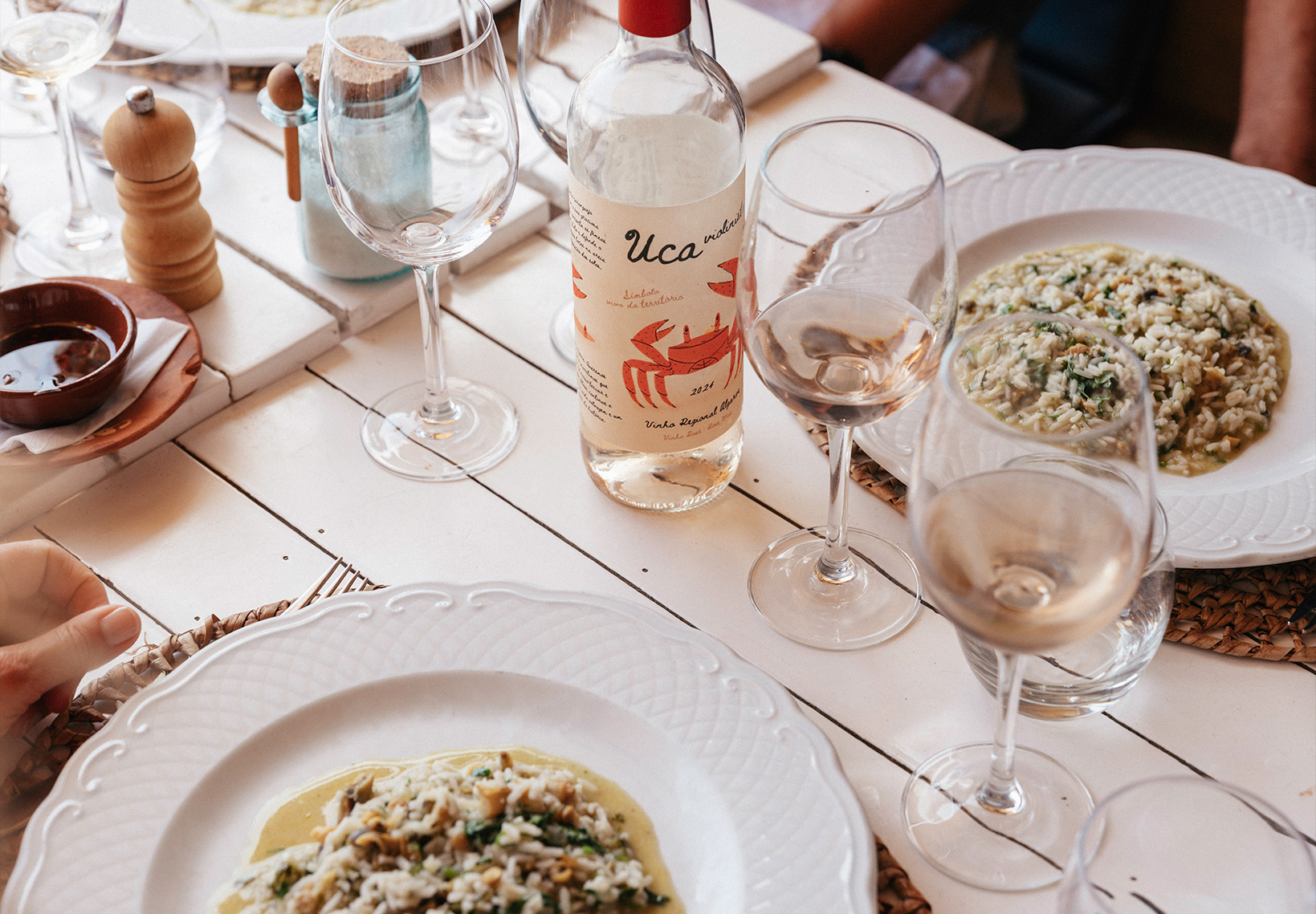 Mesa de restaurante com pratos de arroz de marisco e uma garrafa de vinho branco Uca.
