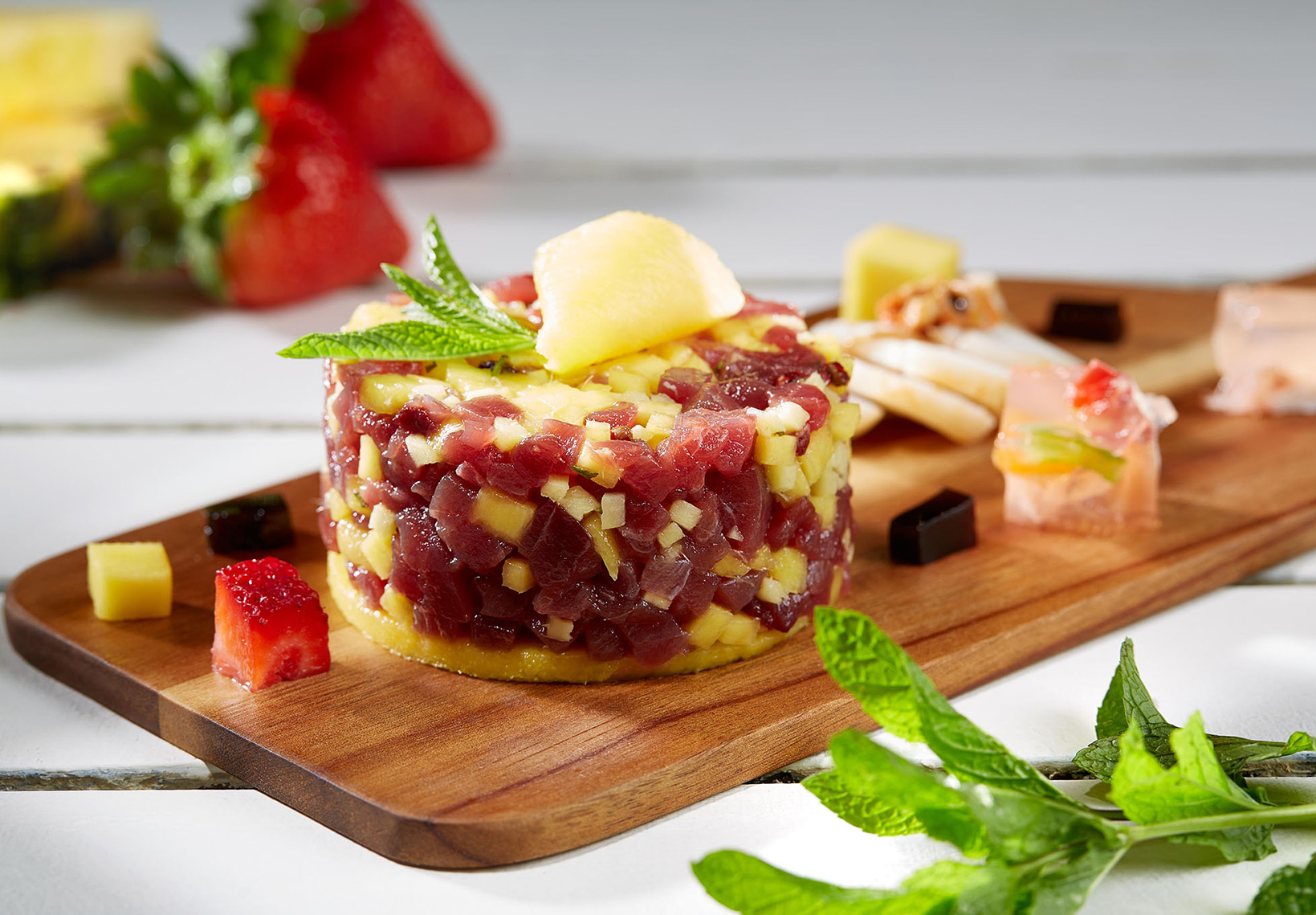 Tártaro de atum e manga apresentado de forma gourmet numa tábua de madeira.