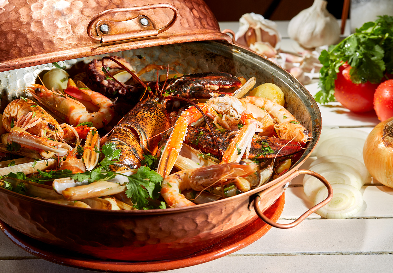 Cataplana de cobre aberta recheada com marisco variado, lagosta e camarões.