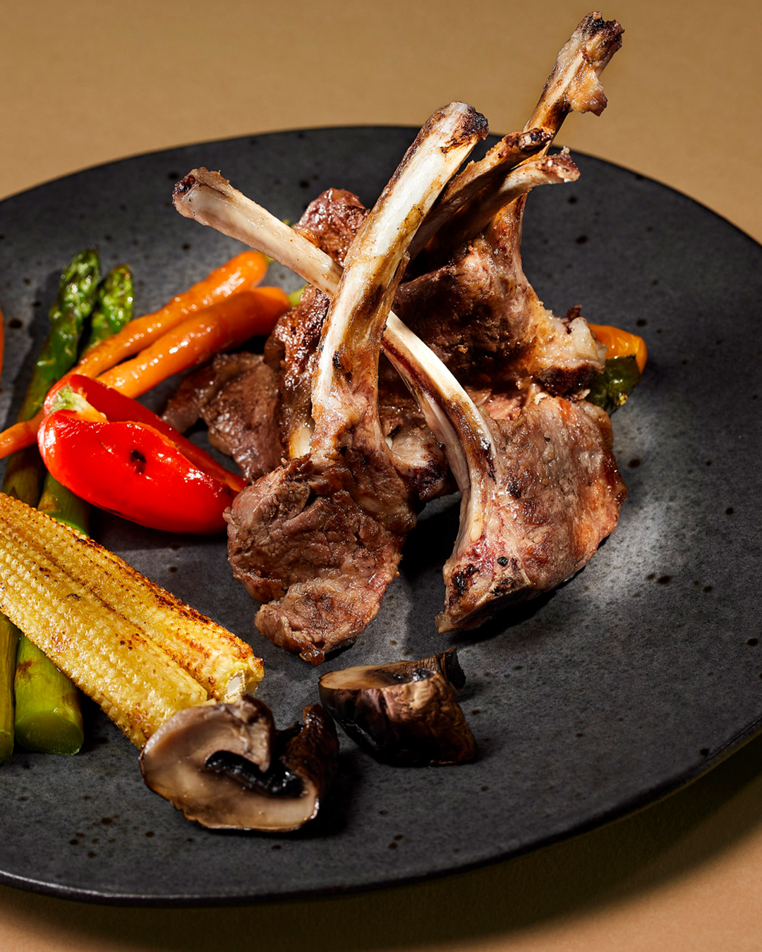 Costeletas de borrego grelhadas servidas com espargos, pimento vermelho e milho baby.