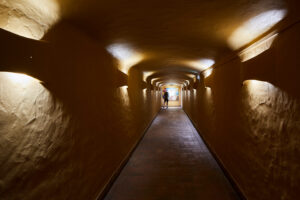 Túnel de acesso iluminado por luzes de parede quentes conduzindo ao restaurante.