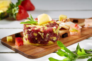 Tártaro de atum e manga apresentado de forma gourmet numa tábua de madeira.